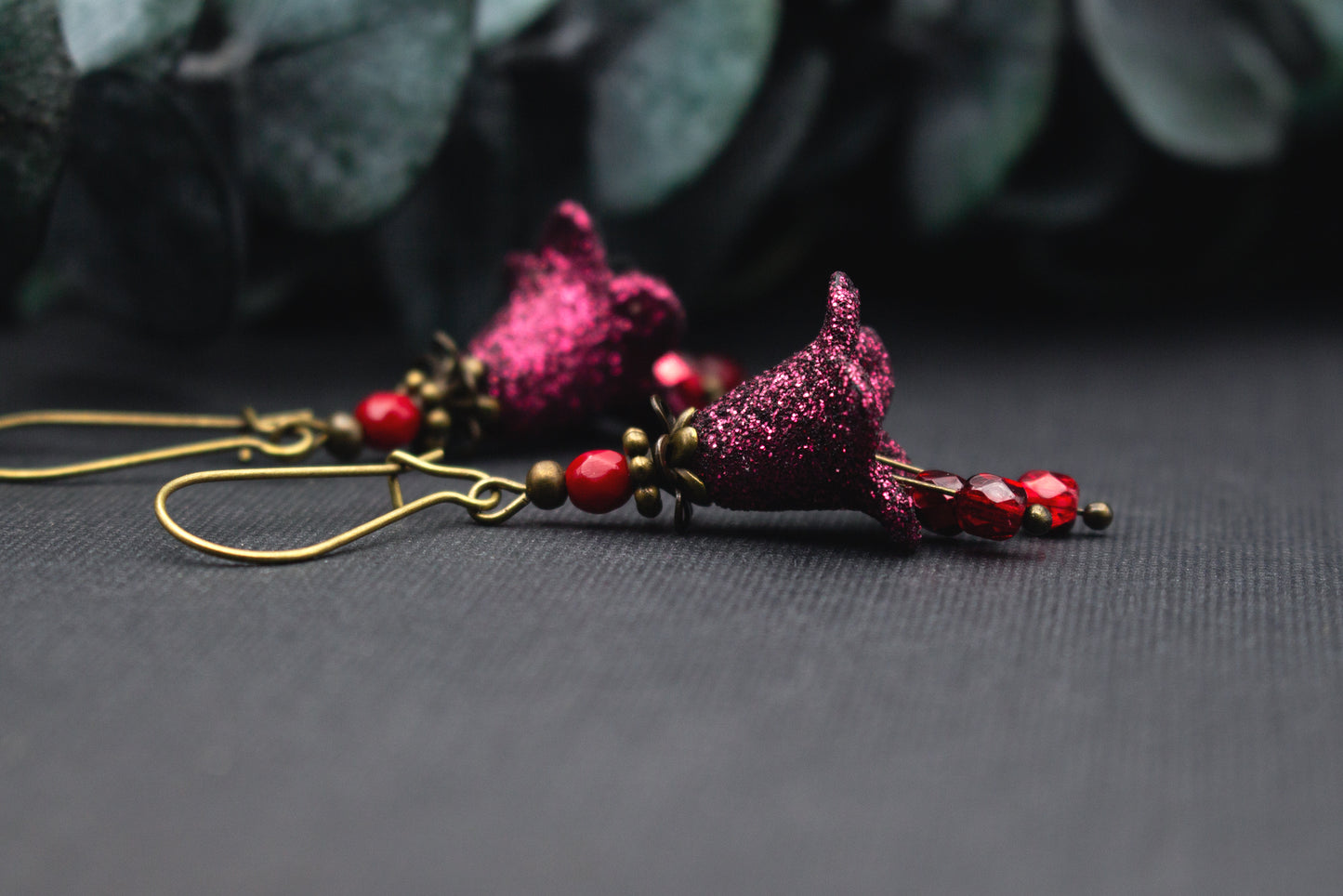 Detailansicht glitzernder Blüte in Fuchsia mit roten Glasperlen an antik-bronzenem Ohrhaken