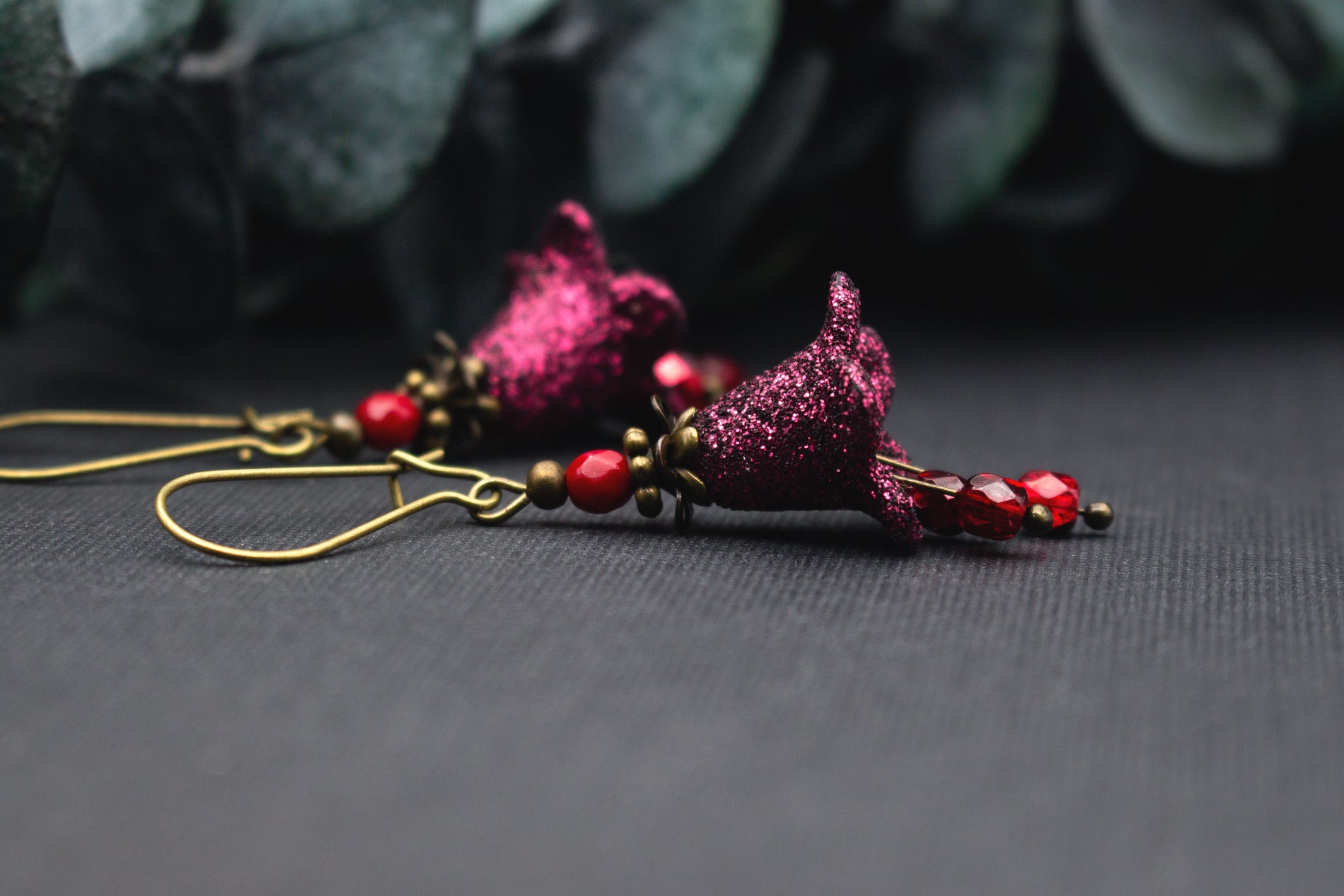 Detailansicht glitzernder Blüte in Fuchsia mit roten Glasperlen an antik-bronzenem Ohrhaken