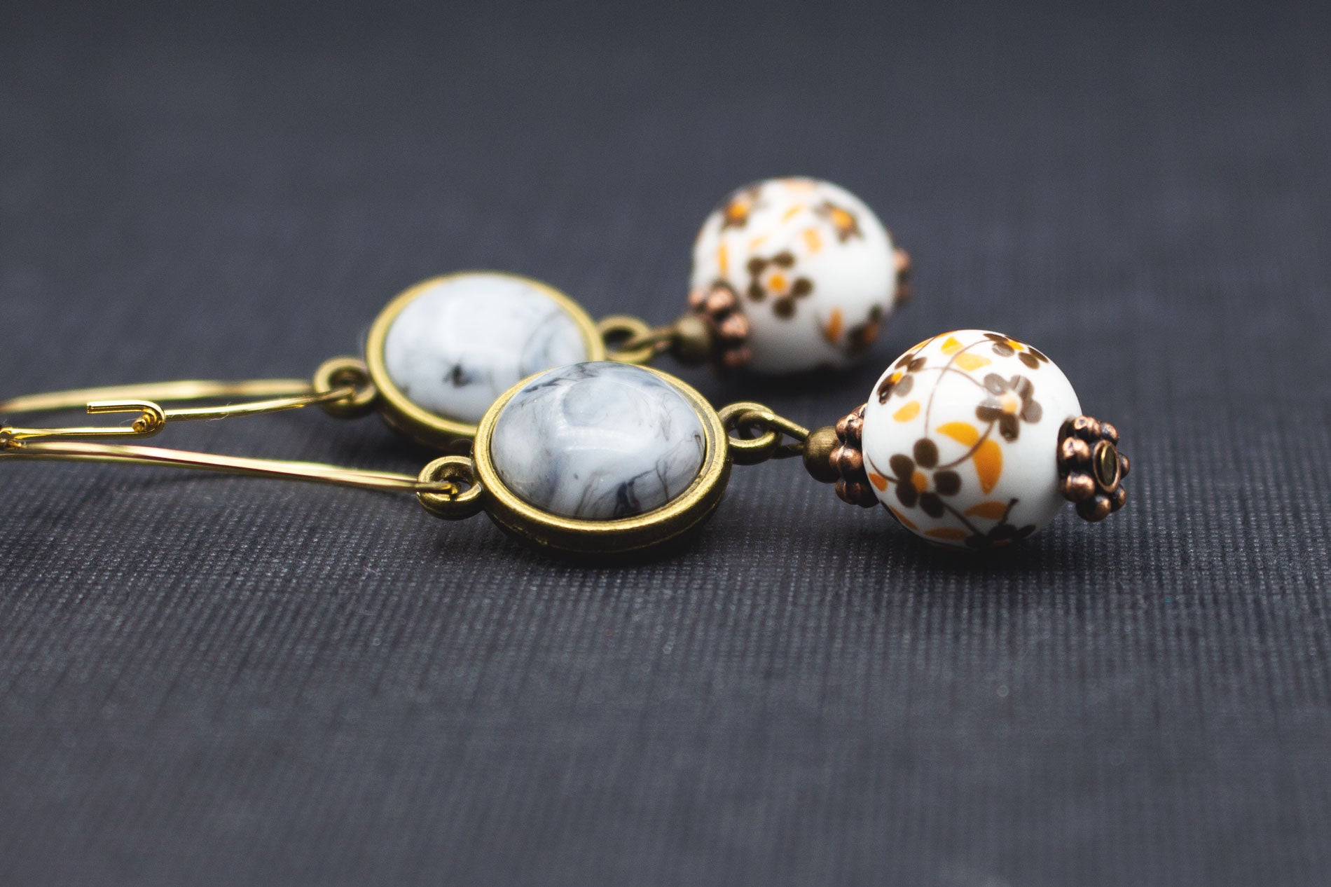 Detail goldfarbene Creolen mit grauen Cabochon-Perlen und floral verzierten Keramikperlen