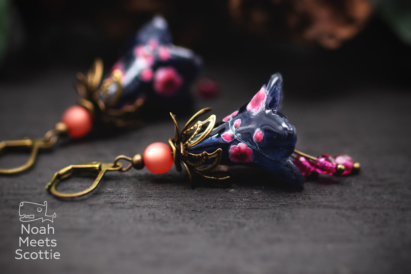 Dunkelblaue Blütenohrringe mit rosa Kirschblüten, pinken Glasperlen und bronzefarbenen Schmuckelementen.