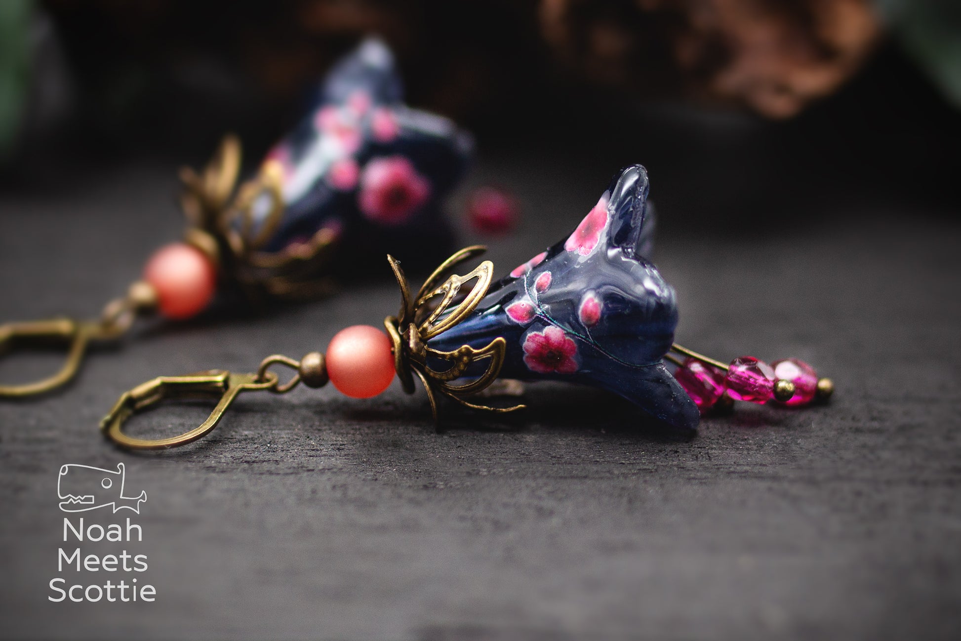 Handbemalte Blumenohrringe in tiefem Nachtblau mit rosa Blüten und leuchtend fuchsiafarbenen Glasperlen.