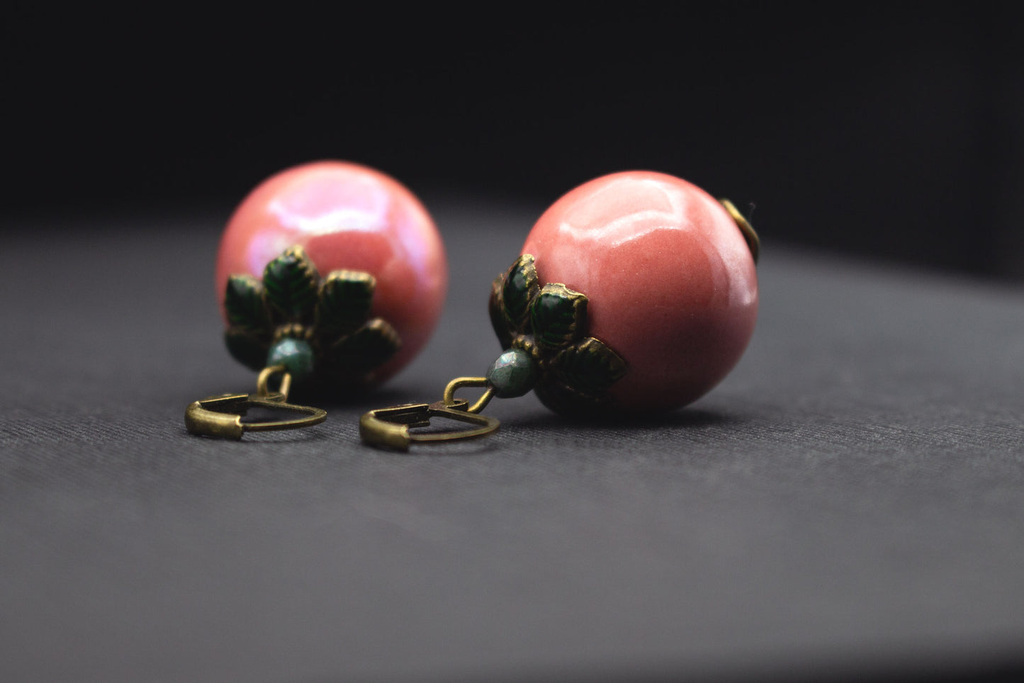 Nahaufnahme roséfarbene Keramikperlen mit dunkelgrünen Blattperlkappen, elegantes Schmuckdesign
