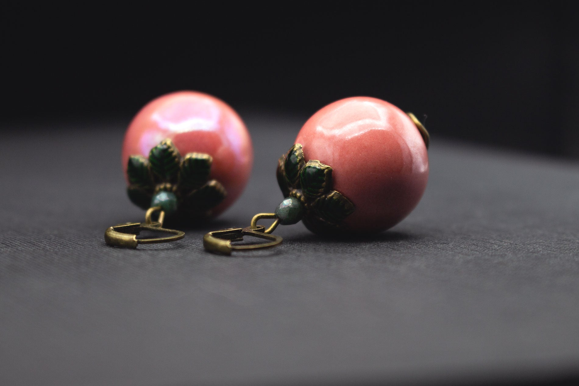 Nahaufnahme roséfarbene Keramikperlen mit dunkelgrünen Blattperlkappen, elegantes Schmuckdesign