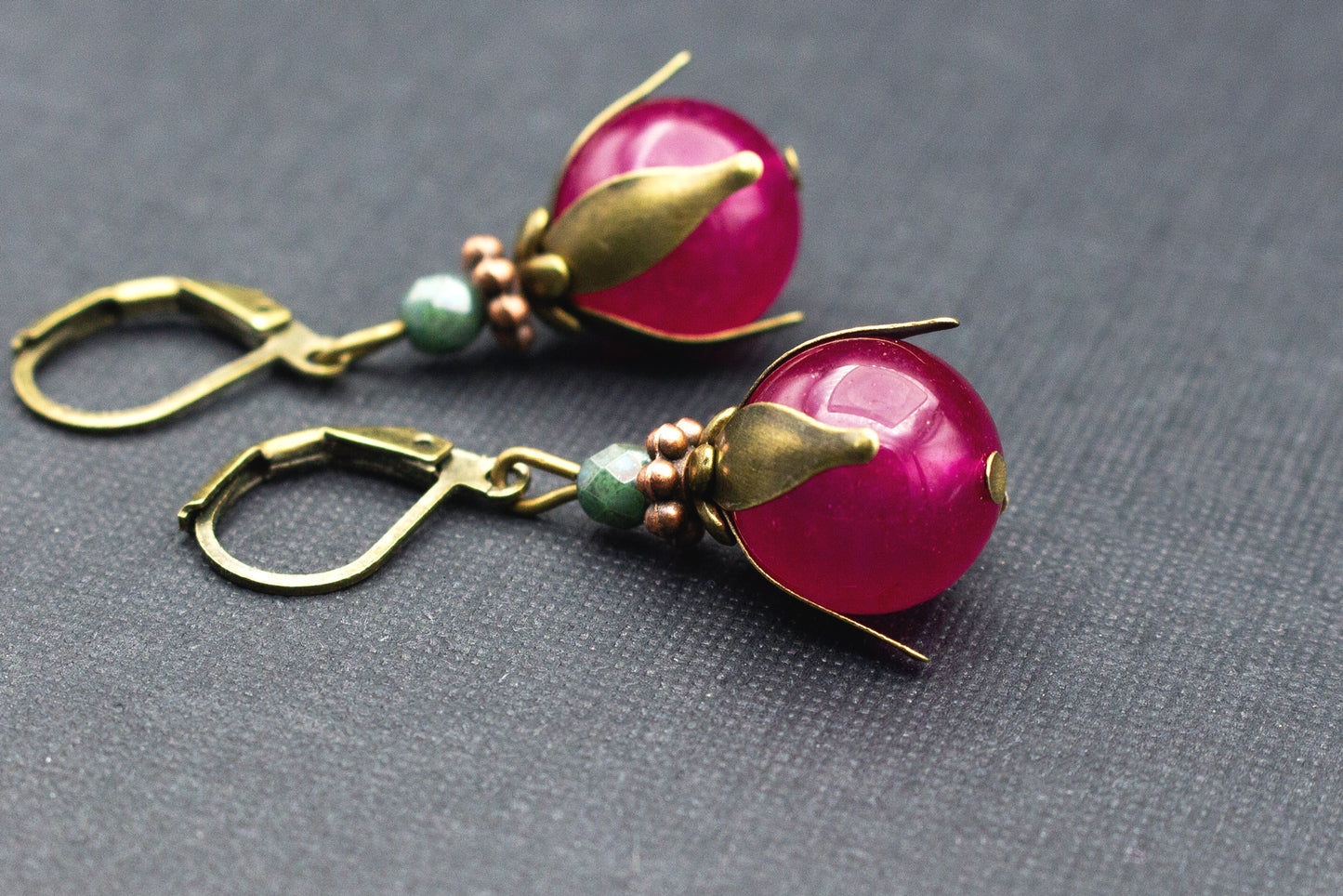 Detailansicht fuchsiafarbener Glasperle mit grüner Akzentperle an antik-bronzenem Ohrhänger