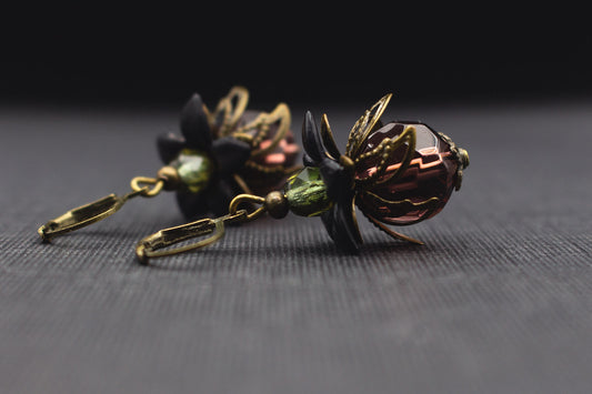 Elegante Ohrringe in Beere-Lila, Schwarz und Lindgrün mit floralen Perlkappen aus Messing auf dunklem Hintergrund.