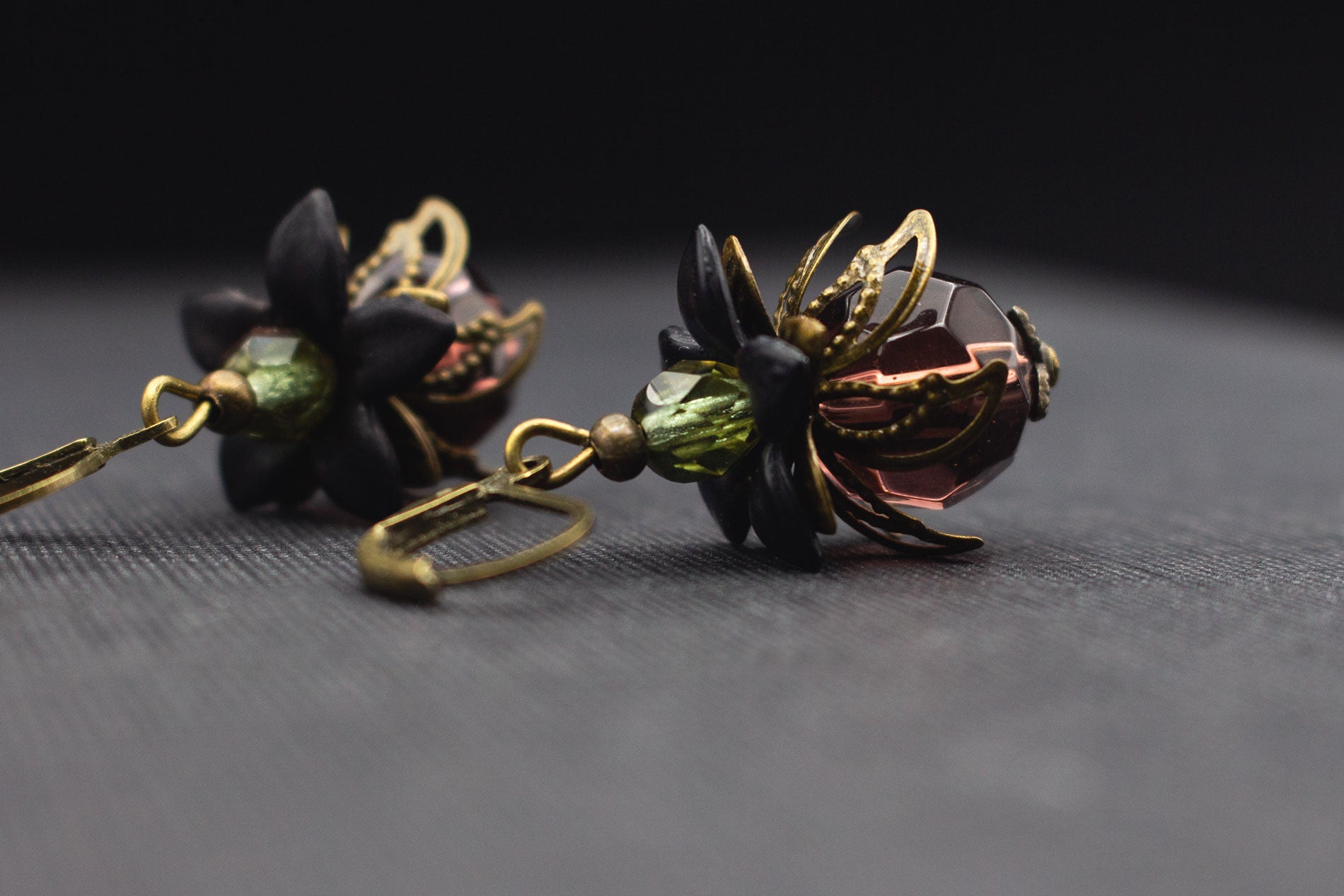 Detailaufnahme von Ohrringen in Beere-Lila, Schwarz und Lindgrün mit goldfarbenen Vintage-Elementen.