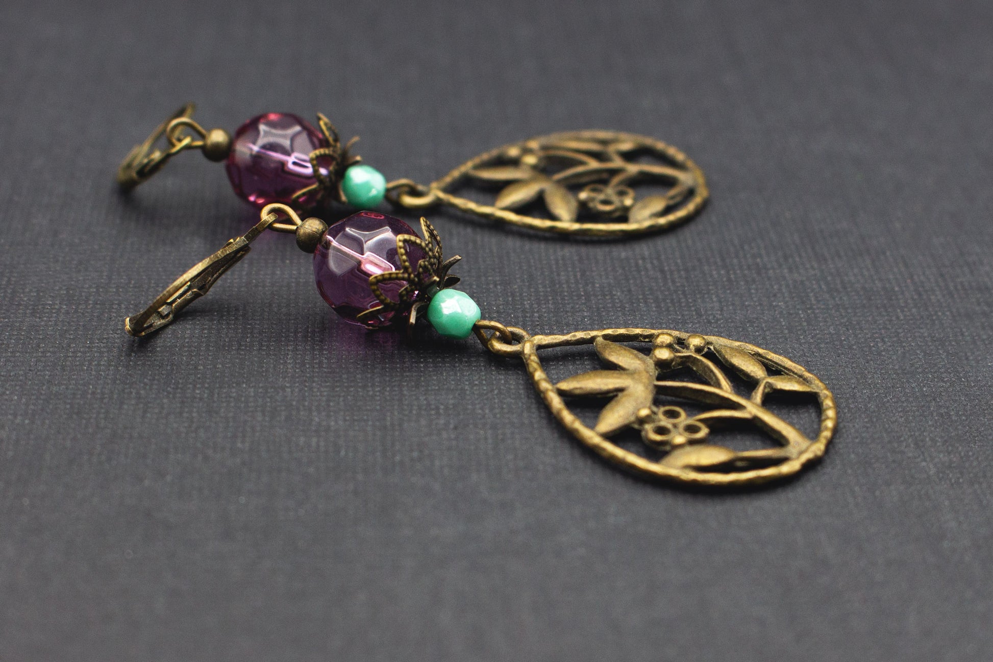 Detailaufnahme von Ohrringen mit violetten Glasperlen, mintfarbenen Perlen und bronzefarbenem Blumenanhänger