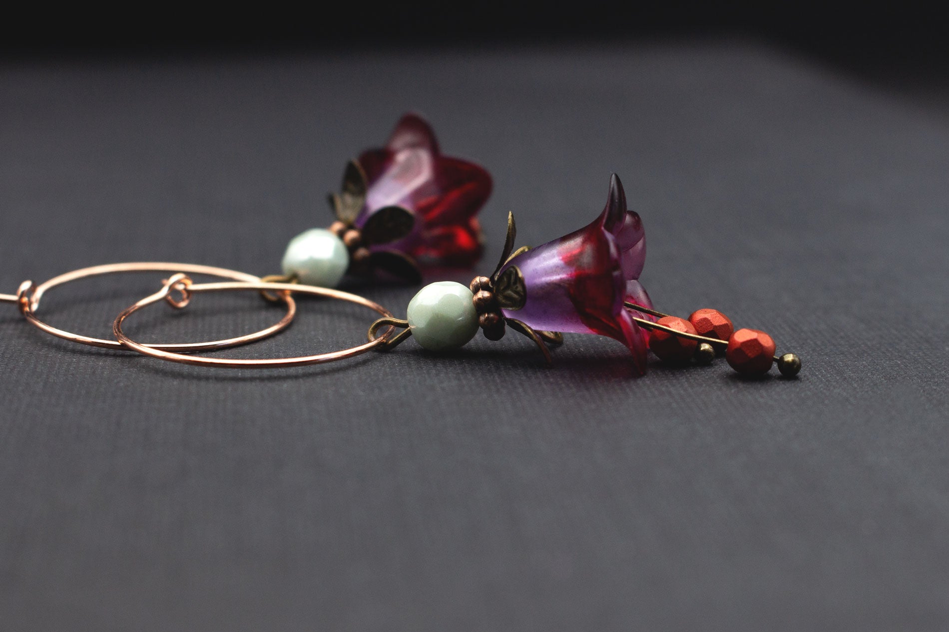 Detailansicht Roségold-Creolen mit lila-roten Acrylblüten und Glasperlen