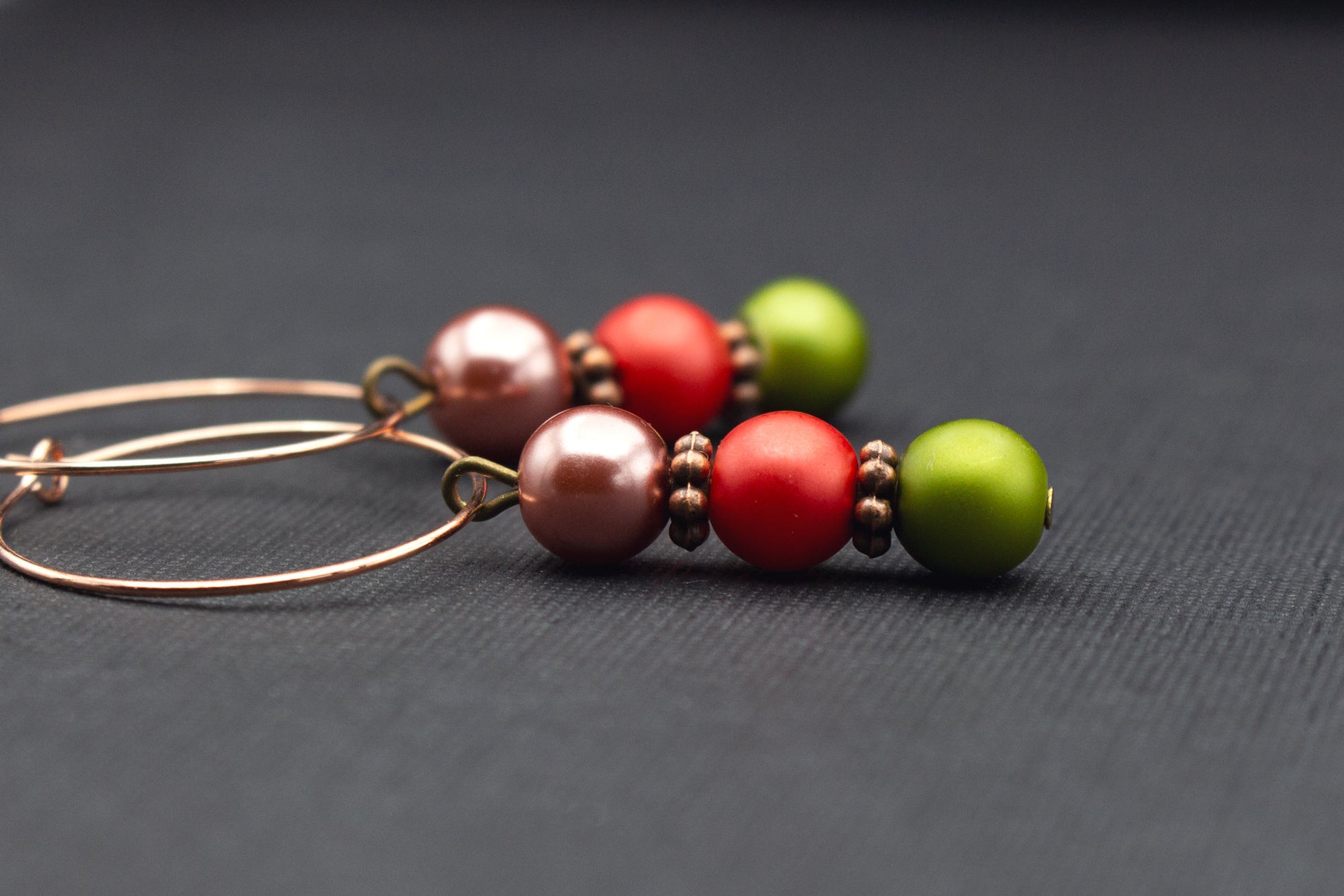 Detailaufnahme von Roségold Creolen mit Perlen in Altrosa, Rot und Olivgrün
