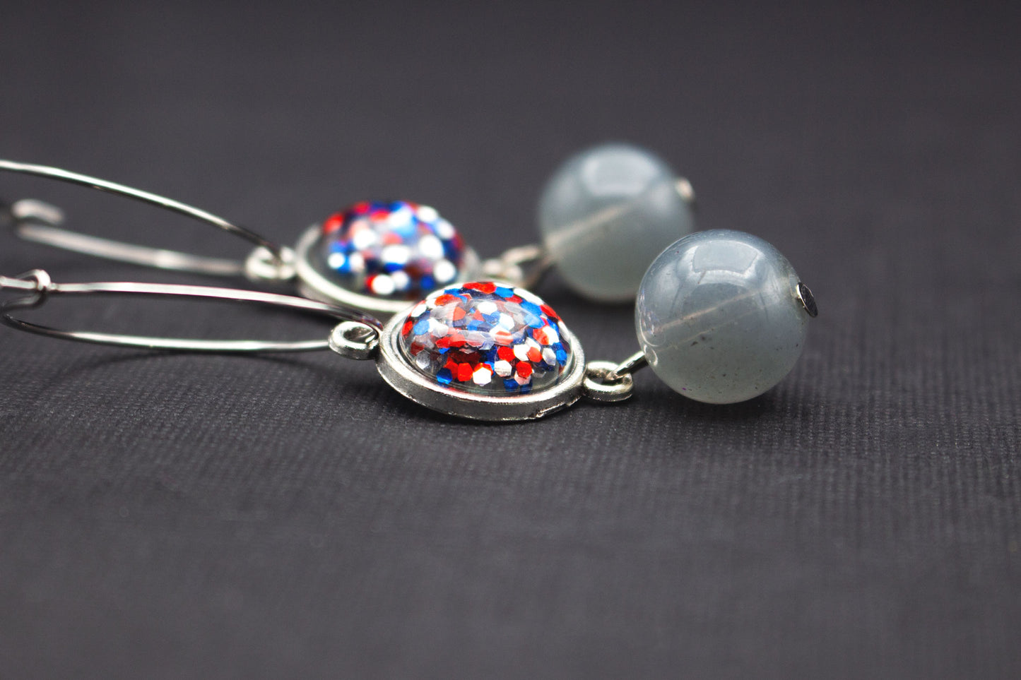 Detailaufnahme silberfarbener Creolen mit Cabochon-Perlen in Rot, Blau und Silber sowie Glasperlen in Rauchgrau