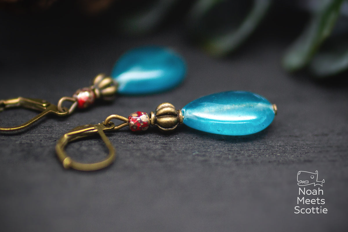 Türkise Ohrhänger im Vintage-Stil mit Tropfenform, roten Details und bronzefarbenem Klappverschluss.